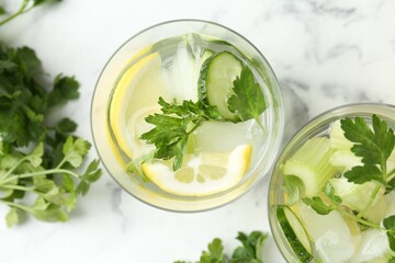 Healthy drink with parsley, cucumbers, lemon and celery on white marble table, flat lay