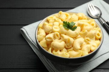 Delicious macaroni and cheese with parsley served on black wooden table, closeup