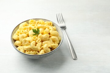 Delicious pasta with cheese sauce in bowl and fork on light table, closeup. Space for text
