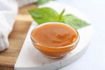 Tasty curry sauce in glass bowl and basil on white table, closeup