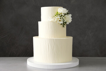 Delicious wedding cake with floral decor on table against grey background