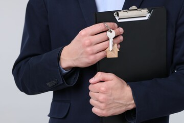 Real estate agent holding key with house shaped keychain and clipboard on light grey background,...