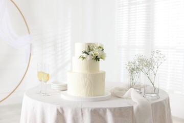 Delicious wedding cake with floral decor and glasses of champagne on table indoors
