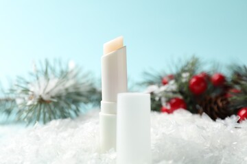 Moisturizing lip balm and Christmas decor on artificial snow against light blue background, closeup. Winter care