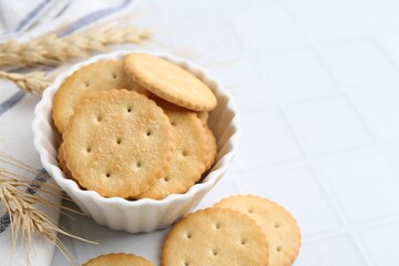 Tasty salty crackers with wheat spikes on white tiled table, closeup. Space for text