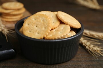 Tasty salty crackers and wheat spikes on wooden table, closeup