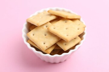 Tasty salty crackers on pink background, closeup
