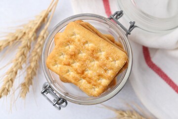 Tasty salty crackers and wheat spikes on white table, flat lay