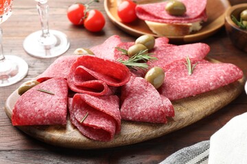 Slices of delicious sausage with olives and rosemary served on wooden table, closeup