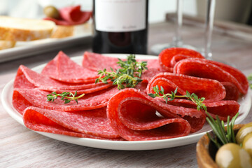 Slices of delicious sausage with thyme served on light wooden table, closeup