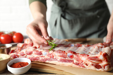 Woman putting rosemary onto raw pork ribs at table, closeup
