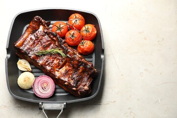 Delicious roasted pork ribs with rosemary, tomatoes and onions on light table, top view. Space for text