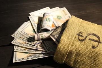 Money bag with dollar banknotes on black wooden table, closeup