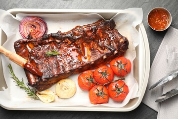 Delicious spare ribs, rosemary, baked onion, sauce and sun dried tomatoes on grey textured table, flat lay