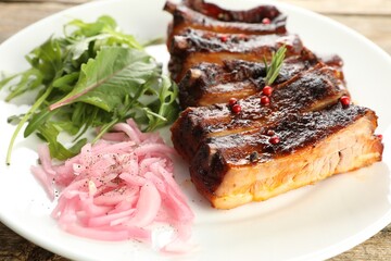 Delicious pork ribs, arugula and onion on wooden table, closeup
