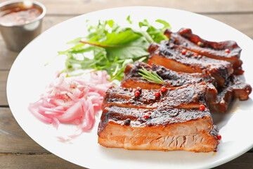 Delicious pork ribs, arugula and onion on wooden table, closeup