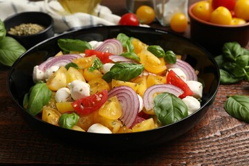 Tasty salad with yellow tomatoes, basil, onion and mozzarella cheese on wooden table, closeup
