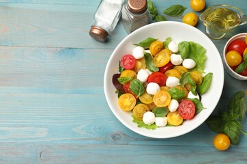 Tasty salad with yellow tomatoes, basil and mozzarella cheese on light blue wooden table, flat lay....