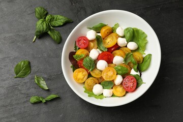 Tasty salad with yellow tomatoes, basil and mozzarella cheese on black table, flat lay