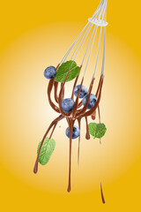 Chocolate cream dripping from whisk and falling blueberries on orange gradient background