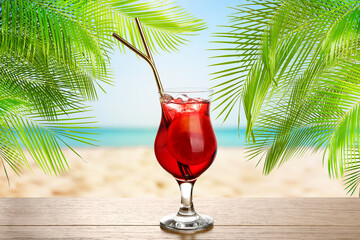 Refreshing cocktail on wooden deck under green palm leaves on tropical beach