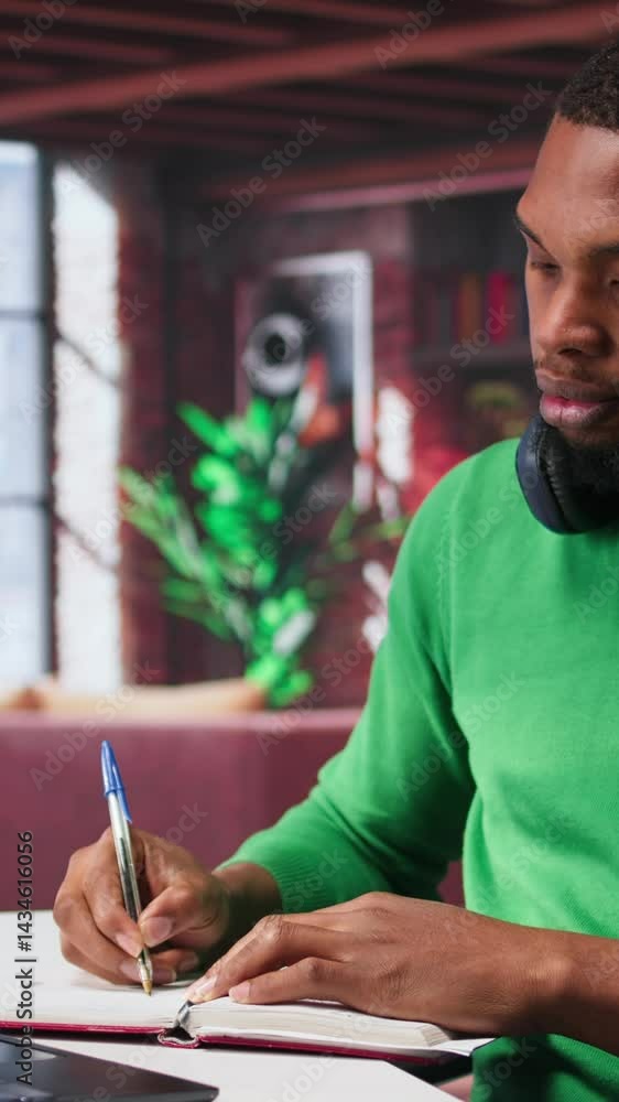 Poster vertical video smiling black man taking notes while watching a tutorial presentation, doing online s