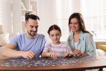 Happy parents and their daughter solving puzzle together at wooden table indoors