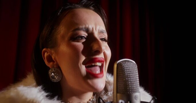 A glamorous woman sings into a microphone while standing on the stage of a theater or opera. Close-up of her face
