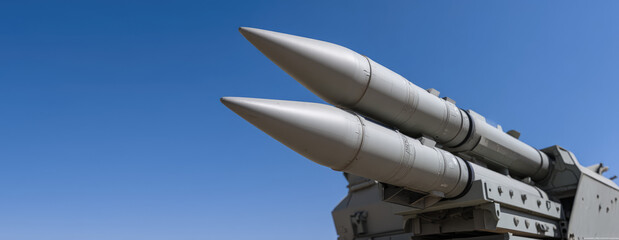 Twin gray missiles mounted on an advanced military launcher system, aimed skywards, under a clear blue sky.  