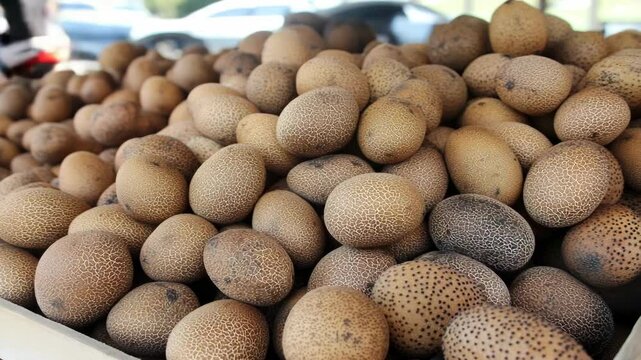 Pile of textured sapodilla fruits displayed for sale at outdoor market, rich brown tone, rough skin, close up view with blurred background.