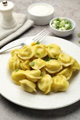 Tasty dumplings with green onion and fork on grey textured table, closeup