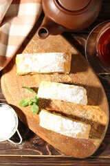Pieces of tasty apple strudel with powdered sugar and mint on wooden table, flat lay