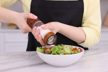 Woman salting tasty salad at white marble table in kitchen, closeup