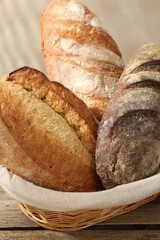 Different loaves of fresh bread in basket on wooden table, closeup