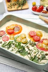 Raw focaccia with vegetables, spices and brush on light grey table, closeup
