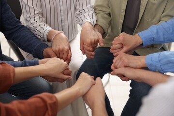 People holding hands during group psychotherapy session indoors, closeup