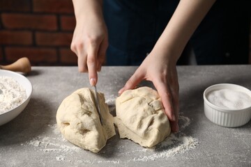 Woman cutting raw dough at light grey table, closeup