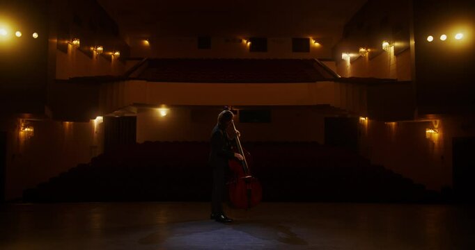 A concert rehearsal on a theater stage in front of an empty auditorium. A man plays the double bass