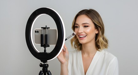 Woman applying makeup in front of a ring light with a phone attached to a tripod stand smiling