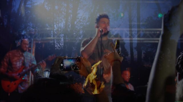 male singer holding mic singing music by campfire, audience raising smartphones, floating notes
