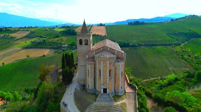 OFFIDA, ITALY - AUGUST 4, 2024: Aerial pullback pedestal up shot of Chiesa di Santa Maria della Rocca. A distancing view of the Church perched on a mountainous cliff, with people, surrounded by nature