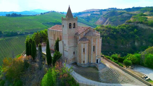 OFFIDA, ITALY - AUGUST 4, 2024: Aerial arcing truck right pan left shot of Chiesa di Santa Maria della Rocca. "Della Rocca" for its strategic cliffside perch, a former Longobard stronghold, fortress