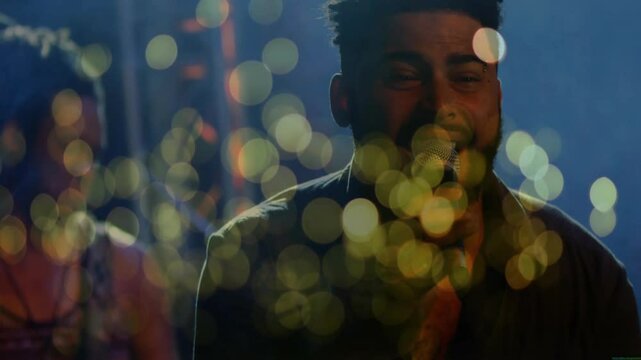 Male singer with bandmate singing on music stage, holding mic and featuring animated bokeh lights
