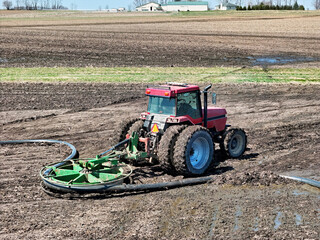 Obraz premium Red tractor using a liquid manure hose mover to assist in field opperations.
