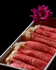 A tray of meat is displayed with a purple flower in the background