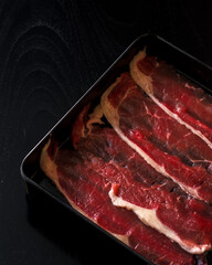 A tray of meat is displayed on a black background