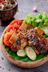 A bowl of food with meat and vegetables, including tomatoes, cucumbers