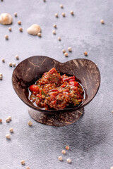 A bowl of food with a red sauce and a few pieces of pepper
