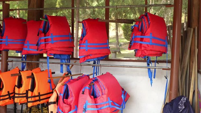 stack of orange and red life jacket for rent, security vest in a recreative outdoors park with a lake