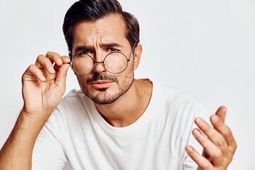 Curious and thoughtful young man wearing glasses looking intently at the camera, gesturing with his hand, isolated on a solid light background. Concept: inquiry and reflection.